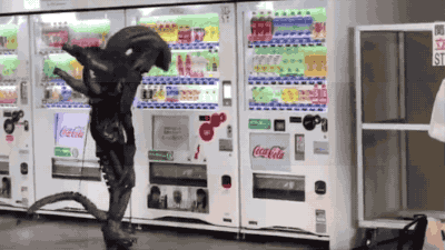 Alien Cosplayer Having Trouble With A Vending Machine