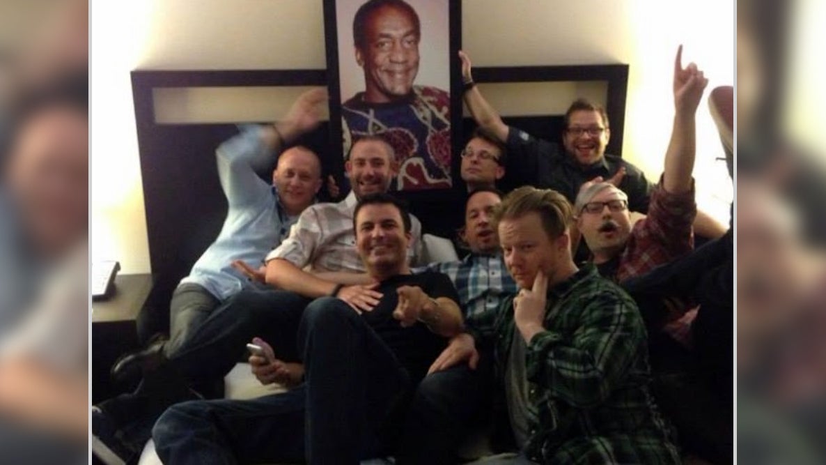 Former World of Warcraft developer Alex Afrasiabi and other current and former Blizzard developers allegedly posing with a portrait of Bill Cosby at BlizzCon 2013.  (Screenshot: Kotaku)