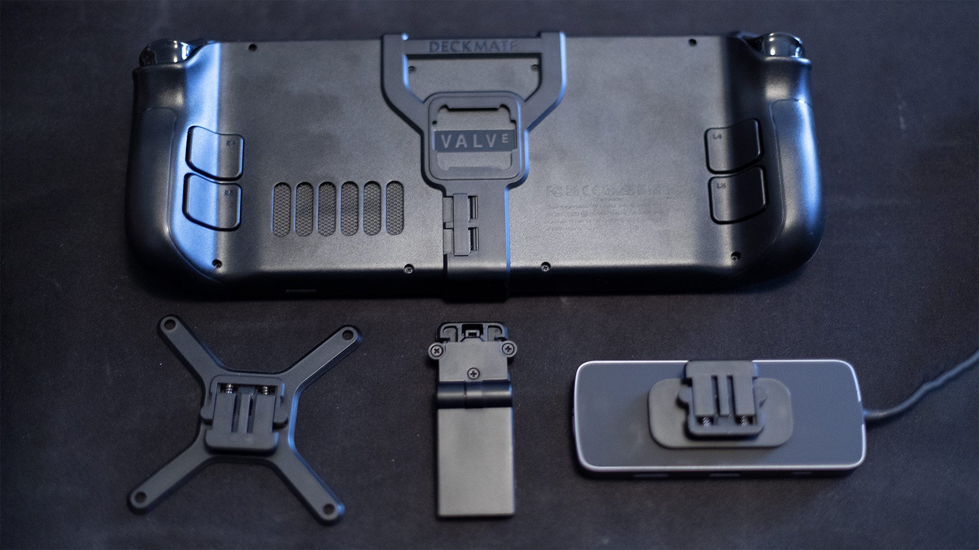 The Steam Deck, with the grip attached, sits next to various Deckmate attachments (the right-most Puck is adhered to a generic USB-C hub). (Photo: Kotaku)